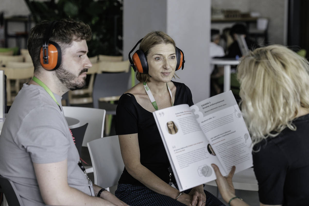 Two people wearing soundproofing headphones listen to the content presented from the booklet by Agata Robinska from the foundation. Close-up of the page with the content of the exercise and quotes.